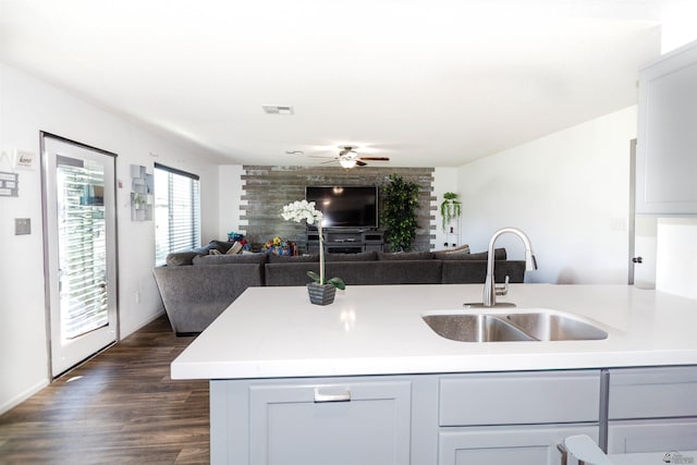kitchen with a sink, open floor plan, ceiling fan, dark wood-style flooring, and light countertops