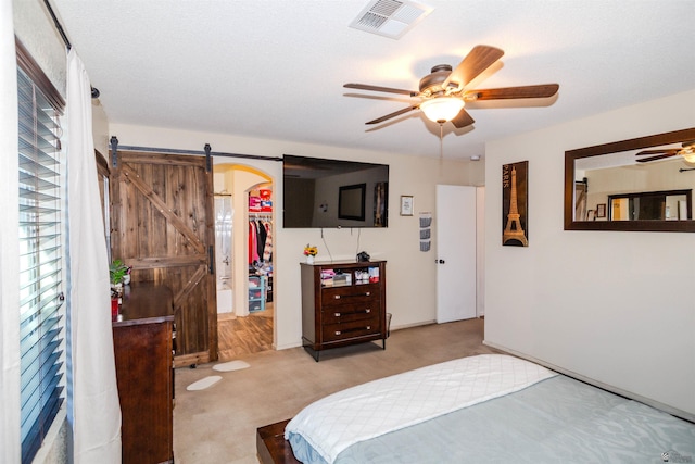 bedroom with a barn door, carpet floors, a walk in closet, ceiling fan, and a closet