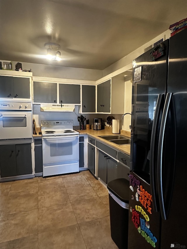 kitchen with gray cabinets, tile patterned flooring, a sink, under cabinet range hood, and white appliances
