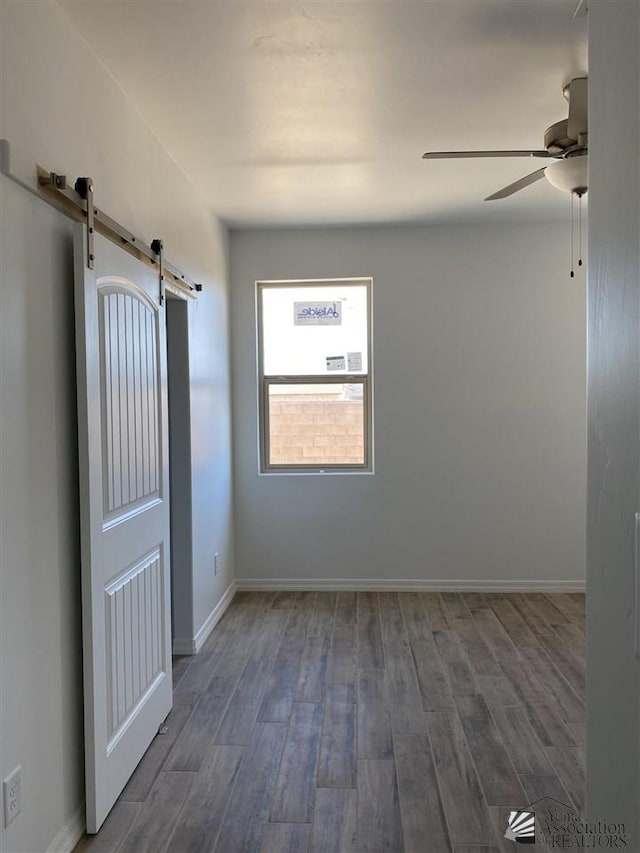 unfurnished room with baseboards, ceiling fan, a barn door, and wood finished floors