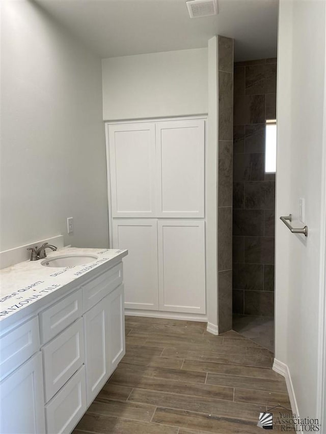 full bath with a walk in shower, vanity, wood finished floors, and visible vents