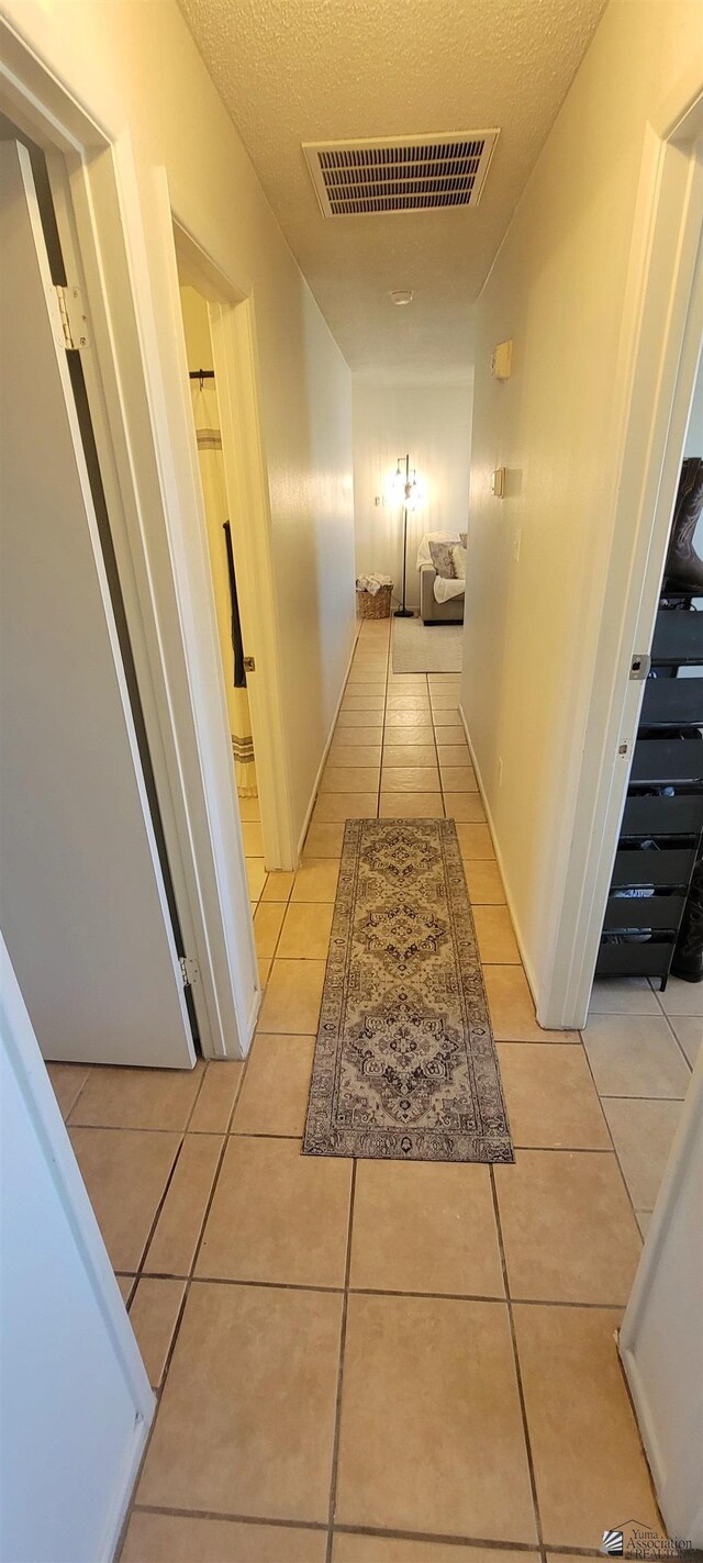 hallway featuring visible vents, a textured ceiling, and light tile patterned floors