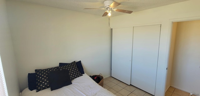 bedroom featuring a closet, a textured ceiling, ceiling fan, and light tile patterned floors