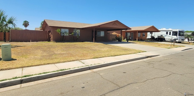 ranch-style house featuring concrete driveway, fence, a front yard, and an attached carport