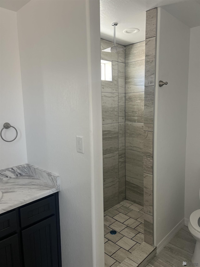 bathroom with toilet, a tile shower, and vanity