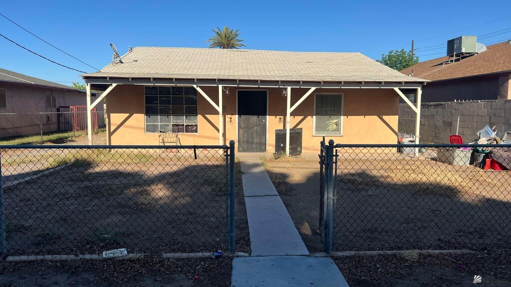 137 S 16th Ave, Yuma, AZ 85364 - view of front of property featuring stucco siding, a shingled roof, a fenced front yard, and central AC