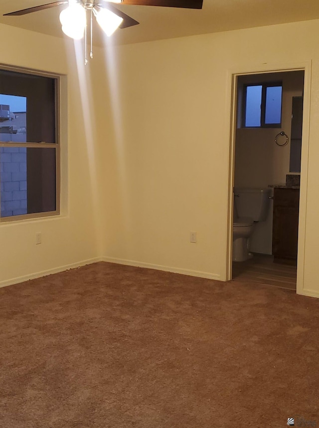 unfurnished room with dark colored carpet, a ceiling fan, and baseboards