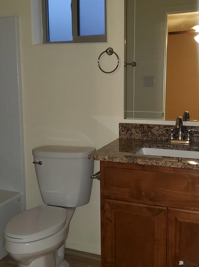 bathroom with a tub, vanity, baseboards, and toilet