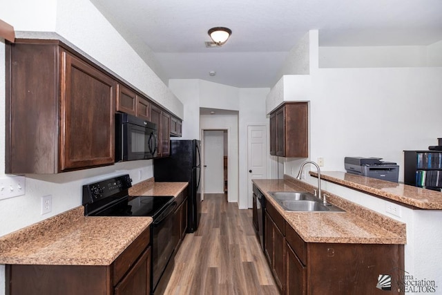 kitchen featuring a peninsula, wood finished floors, dark brown cabinetry, a sink, and black appliances