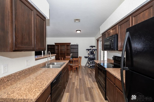 kitchen with a sink, black appliances, wood finished floors, and dark brown cabinets