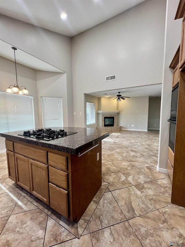 kitchen featuring decorative light fixtures, a kitchen island, a towering ceiling, ceiling fan with notable chandelier, and black appliances