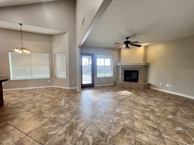 unfurnished living room with lofted ceiling, ceiling fan with notable chandelier, and a tile fireplace