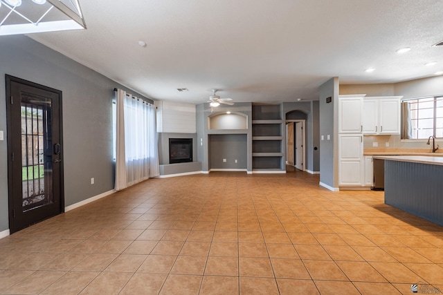 12170 E 33rd Pl, Yuma, AZ 85367 - unfurnished living room featuring light tile patterned floors, a ceiling fan, built in shelves, a glass covered fireplace, and baseboards