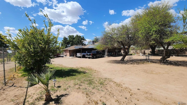 view of front facade with dirt driveway, fence, and a carport