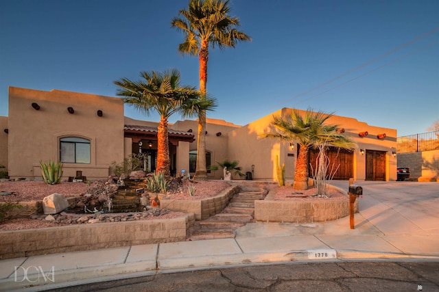 pueblo revival-style home with stucco siding, a tile roof, and concrete driveway