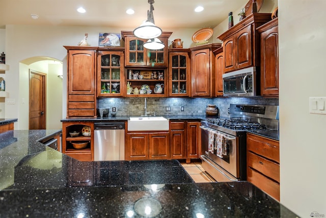 kitchen featuring glass insert cabinets, arched walkways, tasteful backsplash, a sink, and stainless steel appliances