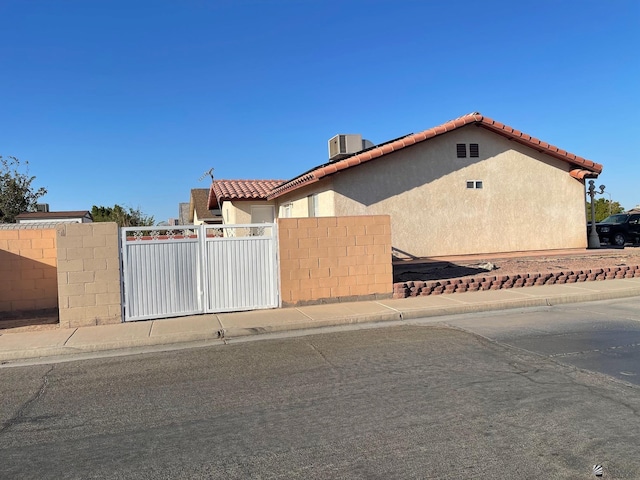 view of front of home featuring fence, central AC, stucco siding, a gate, and a tiled roof
