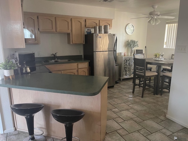 kitchen featuring stone finish floor, ceiling fan, a sink, freestanding refrigerator, and a peninsula