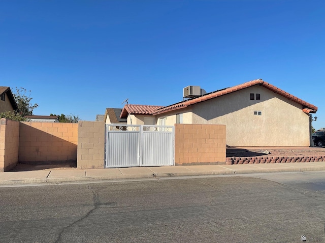 view of front of property with a tiled roof, central AC unit, a gate, fence, and stucco siding