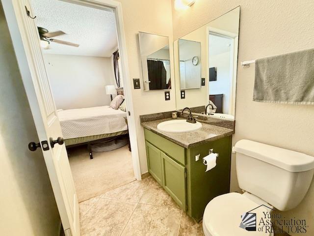 ensuite bathroom with a textured ceiling, ceiling fan, vanity, and toilet