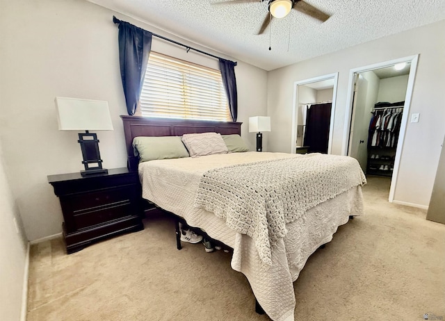 bedroom featuring a textured ceiling, baseboards, a closet, light carpet, and a walk in closet