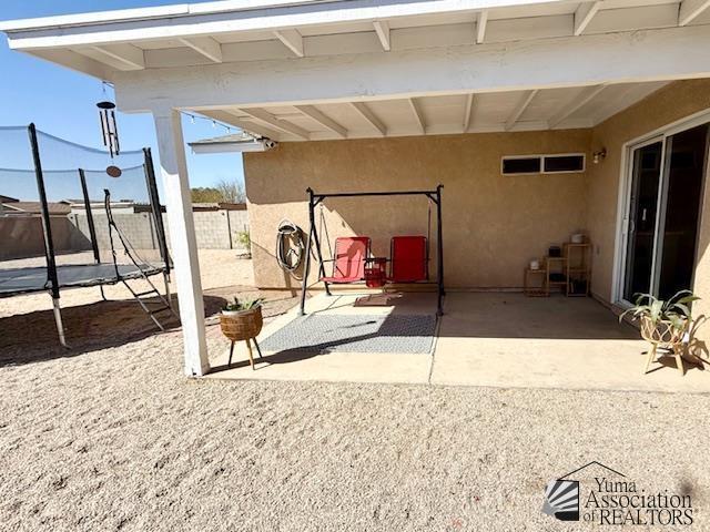 view of patio featuring an attached carport, a trampoline, and fence