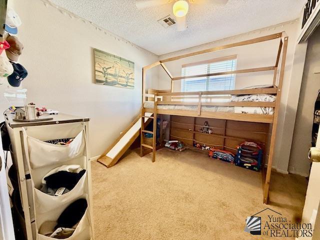 carpeted bedroom featuring visible vents, a textured ceiling, and ceiling fan