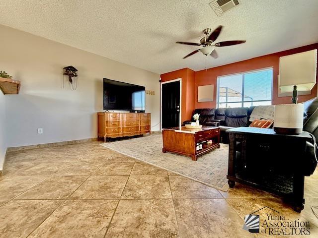 living room with visible vents, baseboards, a textured ceiling, and ceiling fan