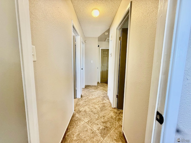 hallway featuring baseboards, a textured ceiling, and a textured wall