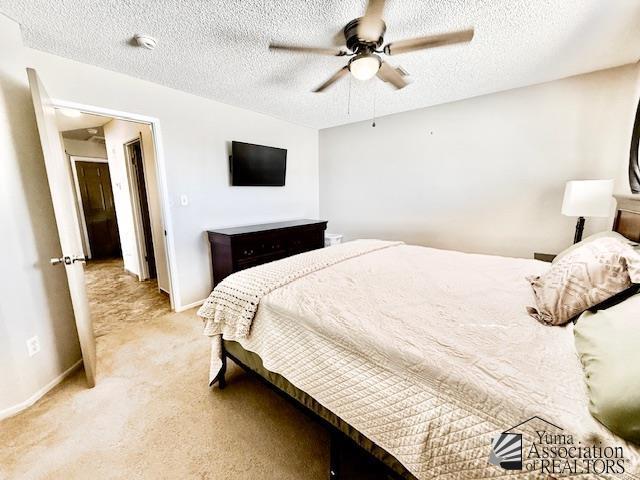 bedroom featuring light carpet, baseboards, a textured ceiling, and a ceiling fan