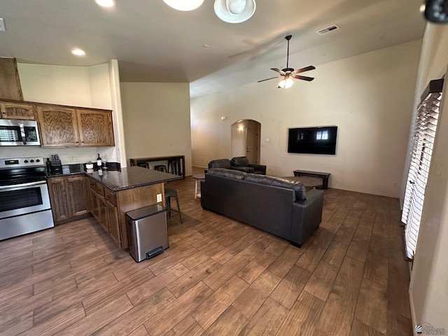 kitchen featuring vaulted ceiling, ceiling fan, appliances with stainless steel finishes, kitchen peninsula, and a breakfast bar area