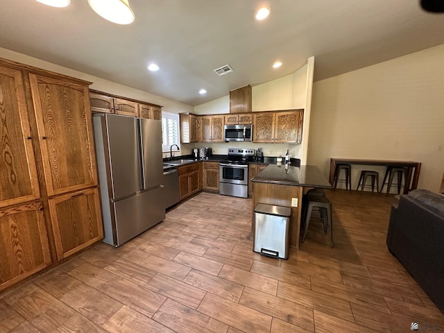 kitchen with sink, vaulted ceiling, a kitchen bar, kitchen peninsula, and stainless steel appliances