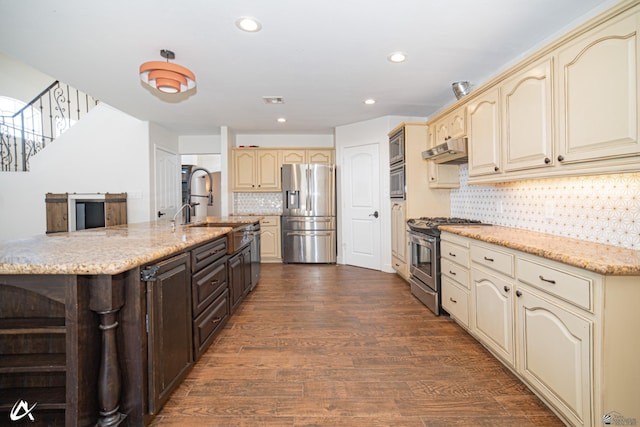 2864 W 12th Ln, Yuma, AZ 85364 - kitchen with appliances with stainless steel finishes, cream cabinetry, under cabinet range hood, dark wood-style flooring, and backsplash