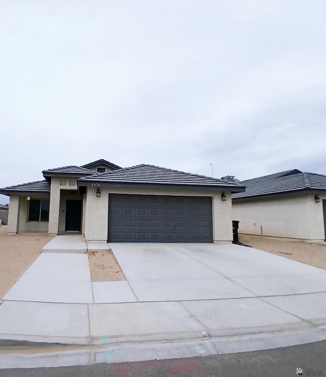 prairie-style home with an attached garage, stucco siding, a tiled roof, and concrete driveway