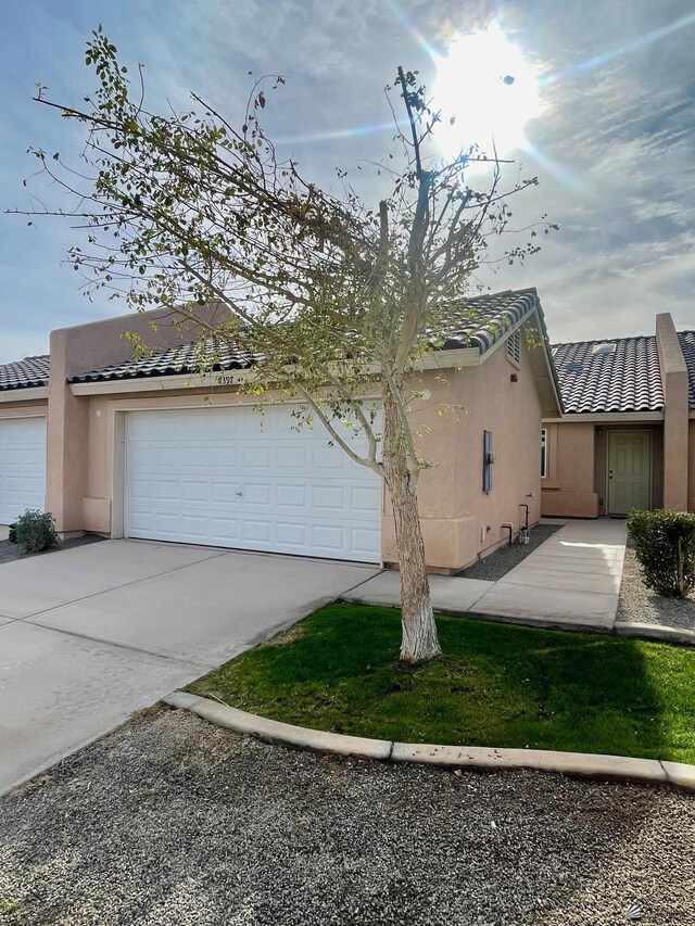 view of side of home with a tiled roof, an attached garage, driveway, and stucco siding