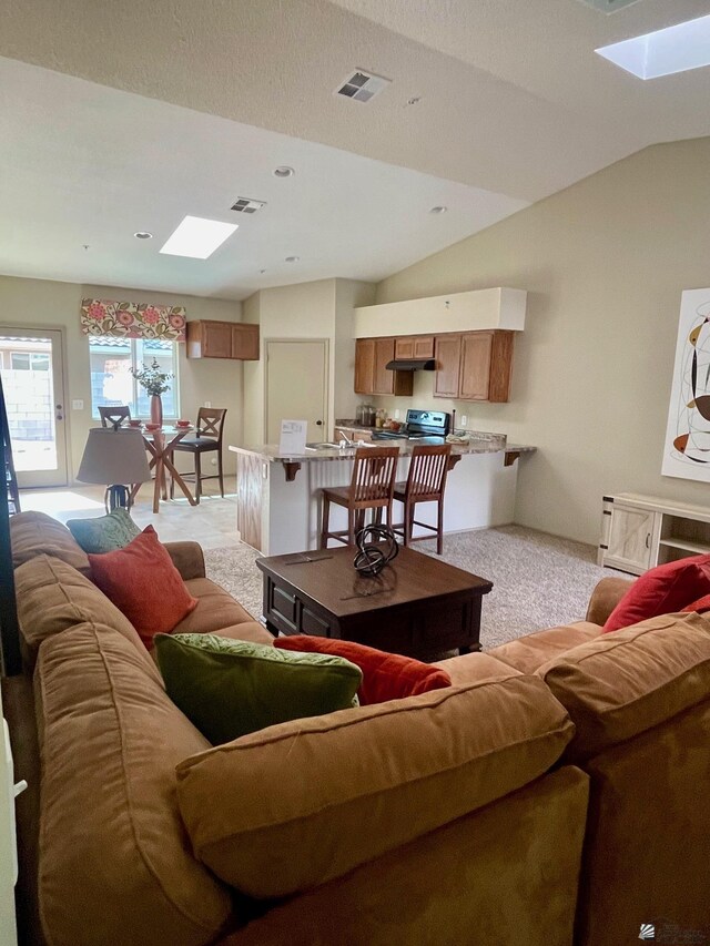 living room featuring visible vents, light carpet, and lofted ceiling with skylight