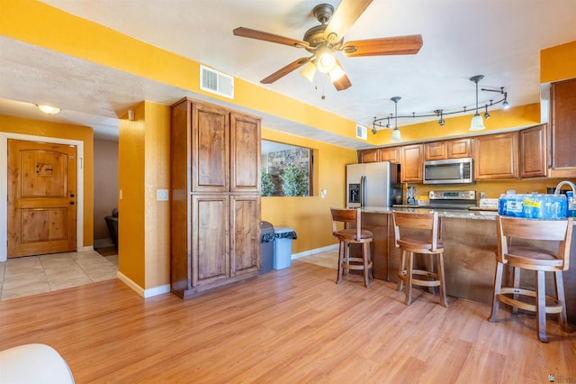 2931 W 20th St, Yuma, AZ 85364 - kitchen featuring appliances with stainless steel finishes, light wood finished floors, brown cabinetry, a breakfast bar area, and a peninsula