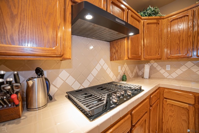 1009 S Tamarack Ave, Yuma, AZ 85364 - kitchen with decorative backsplash, brown cabinets, black gas cooktop, tile counters, and under cabinet range hood