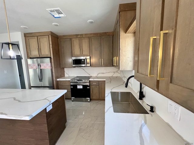 kitchen featuring stainless steel appliances, a sink, light stone countertops, light marble finish flooring, and decorative light fixtures