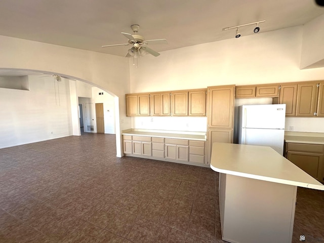 kitchen featuring freestanding refrigerator, ceiling fan, a high ceiling, light countertops, and arched walkways