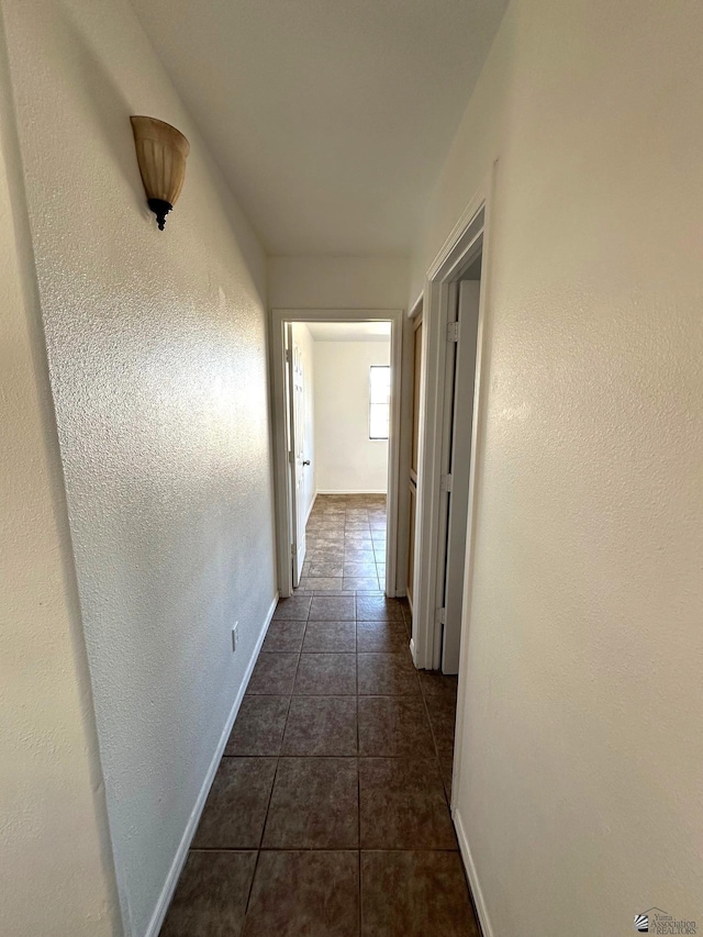 hallway with dark tile patterned floors and baseboards