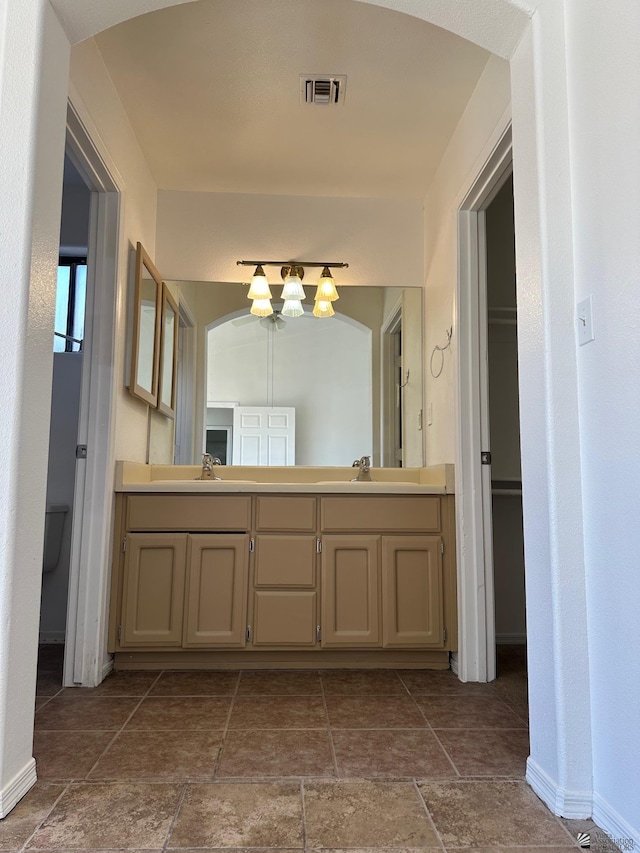 bathroom with visible vents, double vanity, stone tile floors, baseboards, and a chandelier