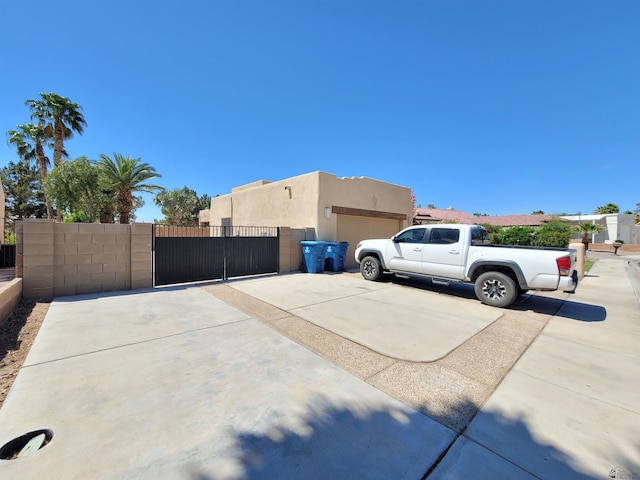 view of property exterior with fence, a garage, stucco siding, a gate, and driveway