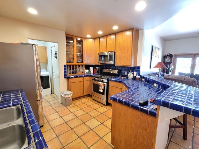 kitchen with appliances with stainless steel finishes, a kitchen breakfast bar, tile countertops, a peninsula, and backsplash