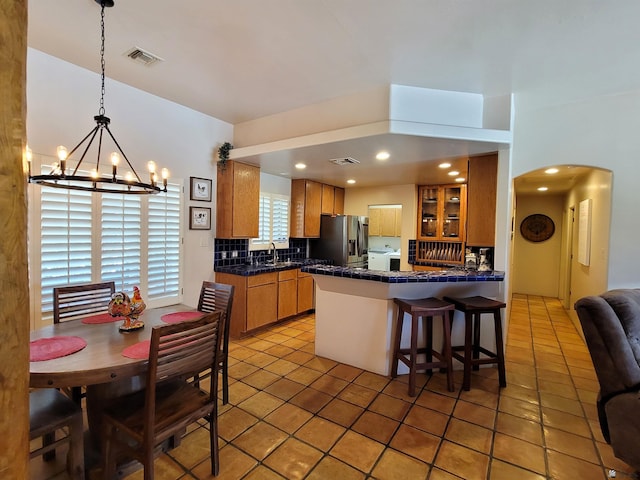 kitchen with visible vents, a peninsula, a kitchen breakfast bar, stainless steel fridge with ice dispenser, and arched walkways