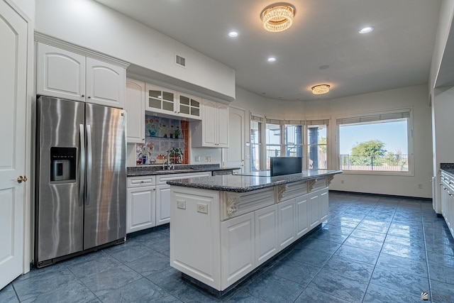 kitchen with visible vents, a kitchen island, glass insert cabinets, stainless steel fridge, and white cabinets