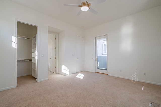 unfurnished bedroom with a spacious closet, baseboards, a ceiling fan, and light colored carpet