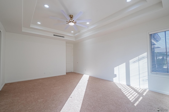 spare room with a raised ceiling, ceiling fan, light colored carpet, and visible vents