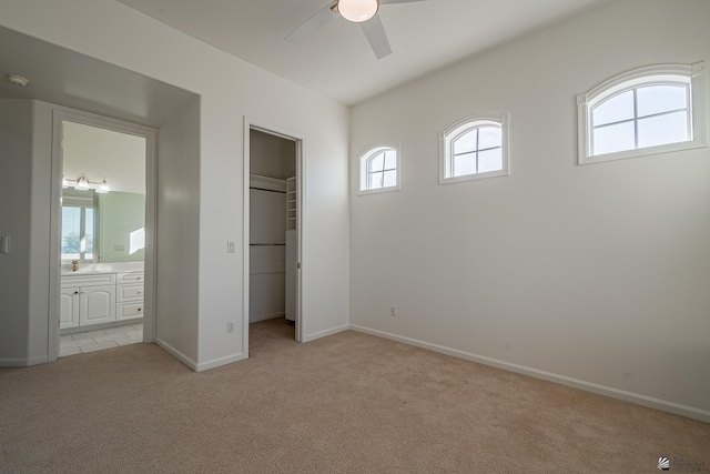 unfurnished bedroom featuring connected bathroom, baseboards, light colored carpet, and a walk in closet