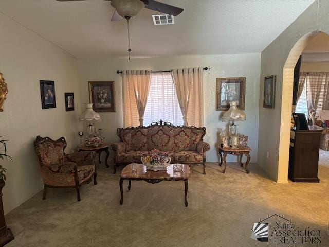 living area featuring arched walkways, a ceiling fan, light colored carpet, and visible vents